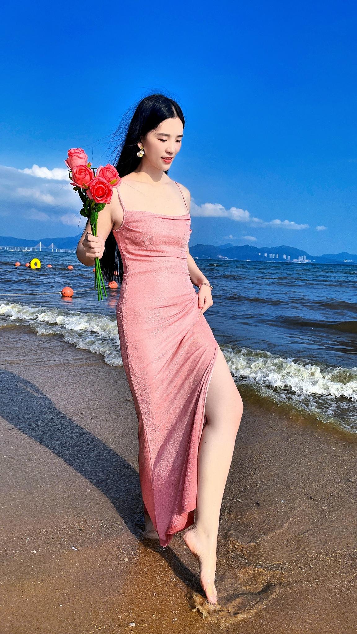 海风拂过裙摆，浪花轻吻脚踝，手里捧着玫瑰，就像是从童话里走出的主角。这一袭粉色长