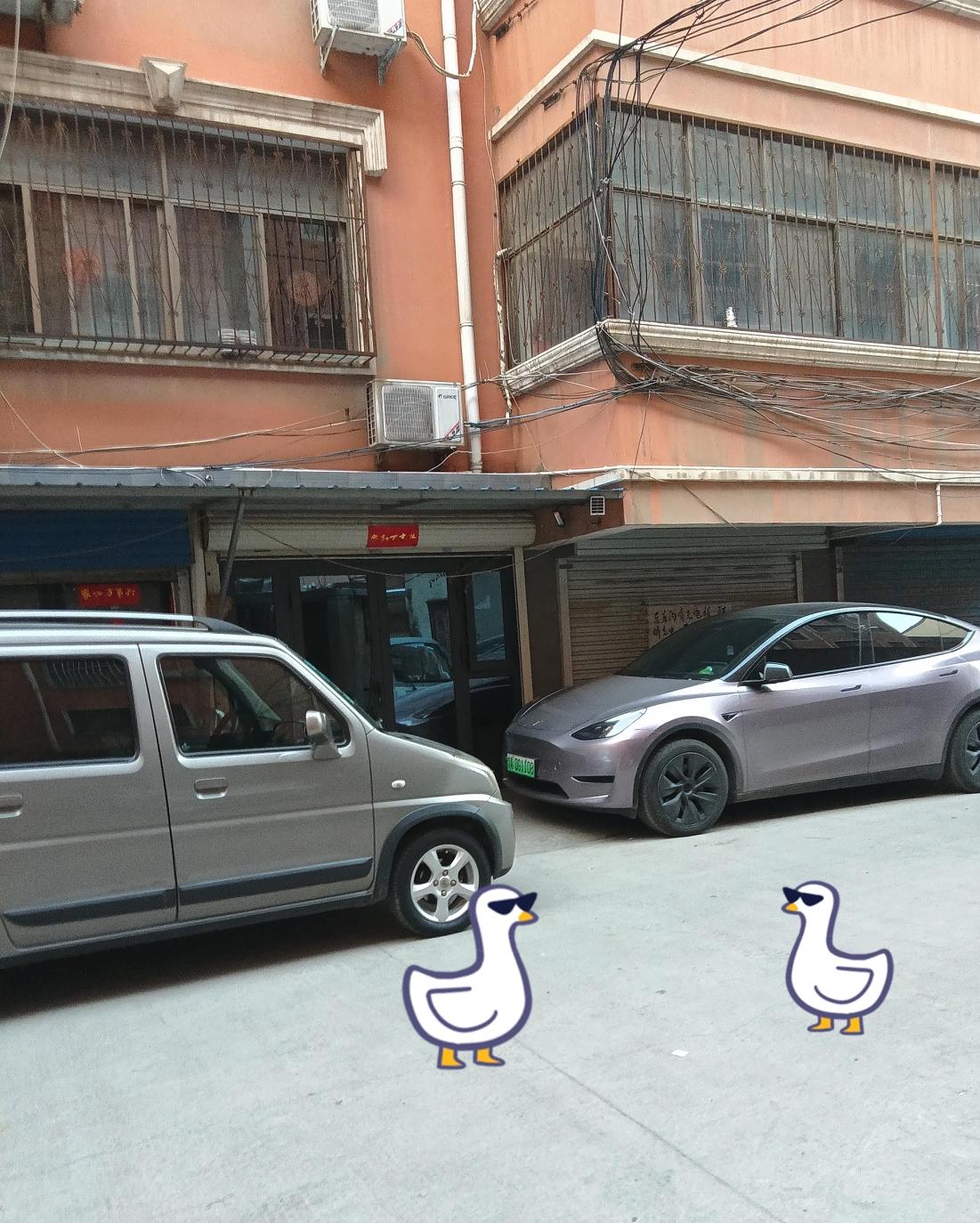 这是一栋外墙呈橙红色的居民楼，窗户都装着铁栅栏。楼前停着两辆车，一辆是银灰色的五