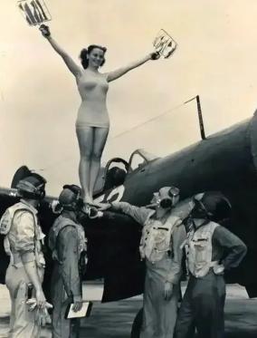 1942年，一个美丽的女性身影优雅地站在战斗机的翅膀上，四个飞行员正在向她抬头瞭