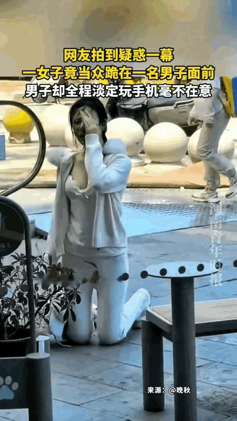 穿搭时尚的年轻女士用手捂着脸放低姿态，给一位男士街头下跪乞求原谅，男士则是坐在她
