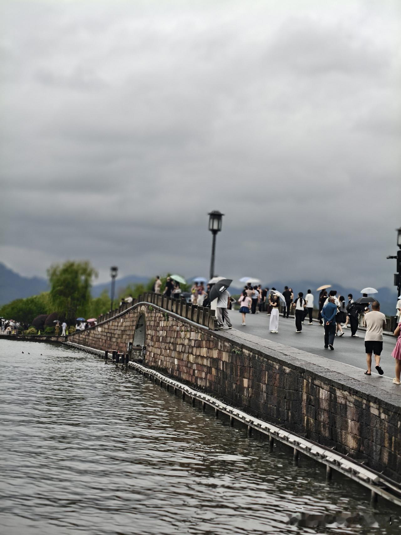 阴雨天的西湖，自带一层温柔滤镜。古桥上行人往来，湖面荷叶田田，远山在云雾里若隐若