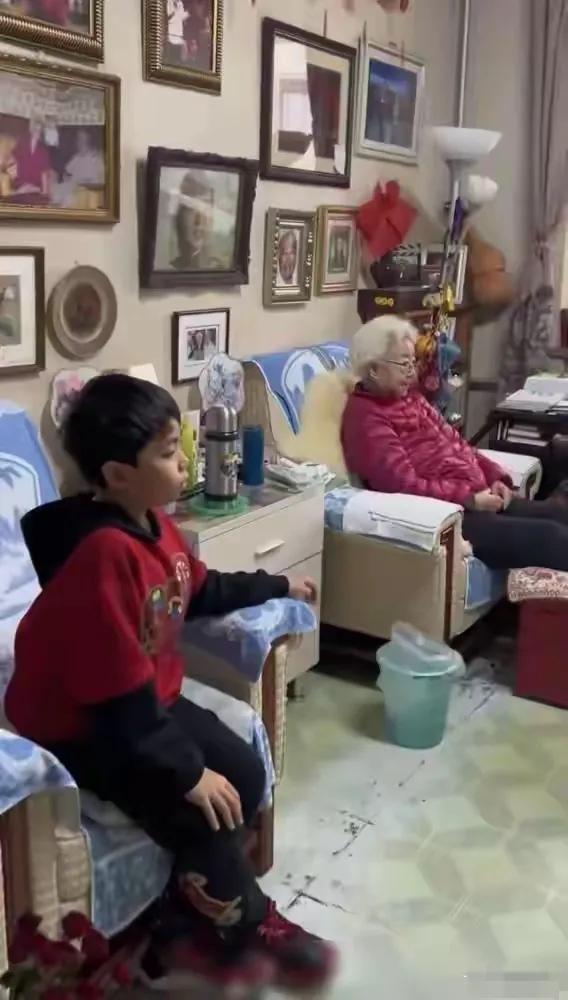 这是老艺术家田华在家中的情景，屋里空间并不大，显得有些狭小，小孙子也在跟她一起观