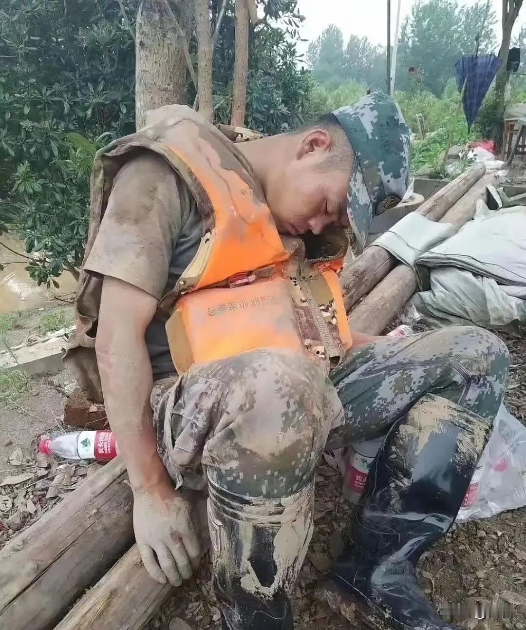 这张照片让无数人泪崩，一个满身淤泥的战士，累的靠在一棵树旁睡着了。

他手里还攥
