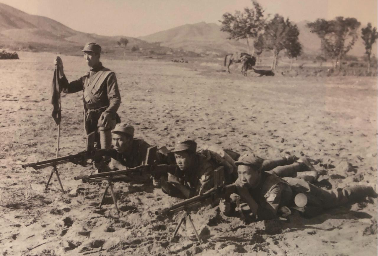 这是抗战时期（1938年）八路军战士的训练老照片。一名指挥员持旗指挥，三名战士卧