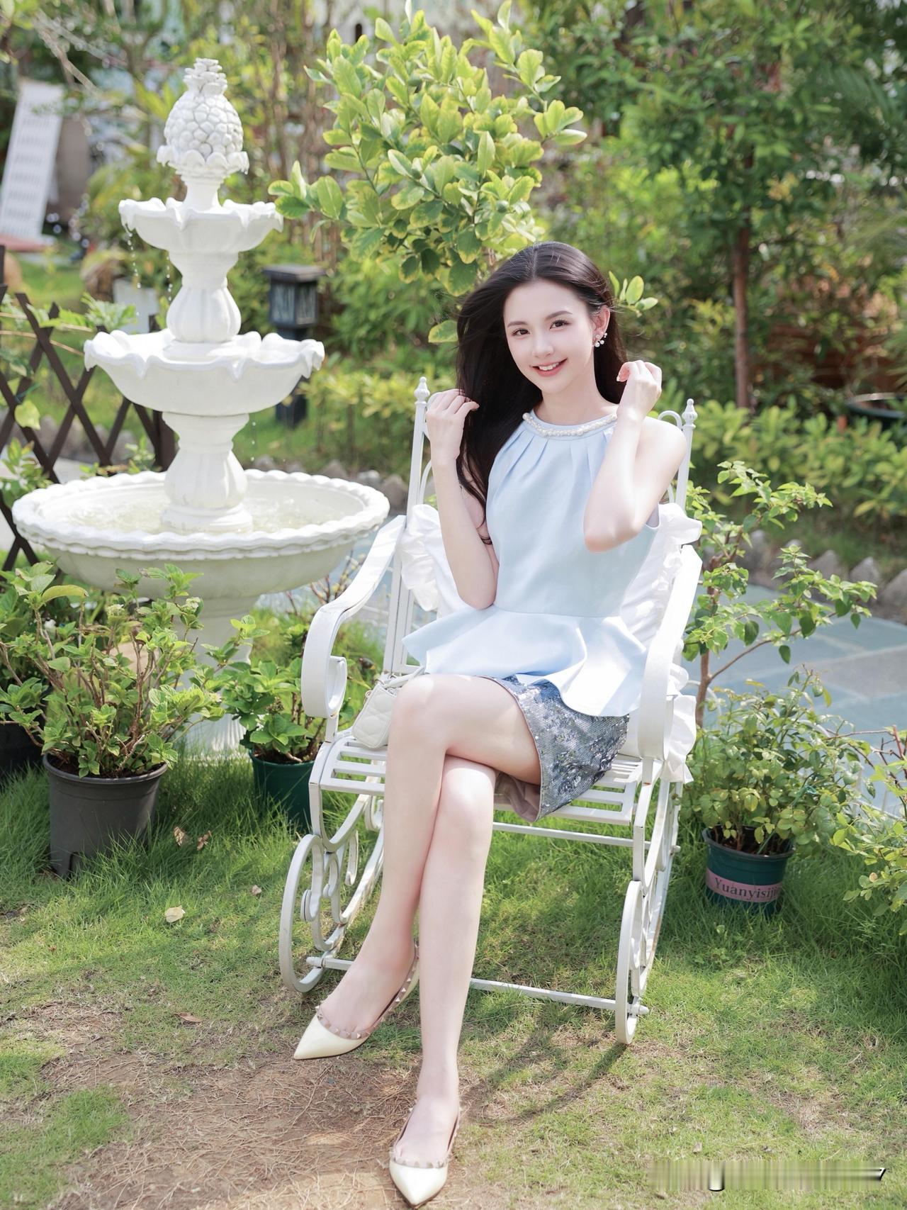 夏日花园里，优雅的蓝裙少女与白色喷泉相伴，清新自然。