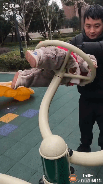 一名幼童被一名男子塞进健身圆盘，男子猛地转动圆盘，幼童随之快速旋转。男子脸上满是