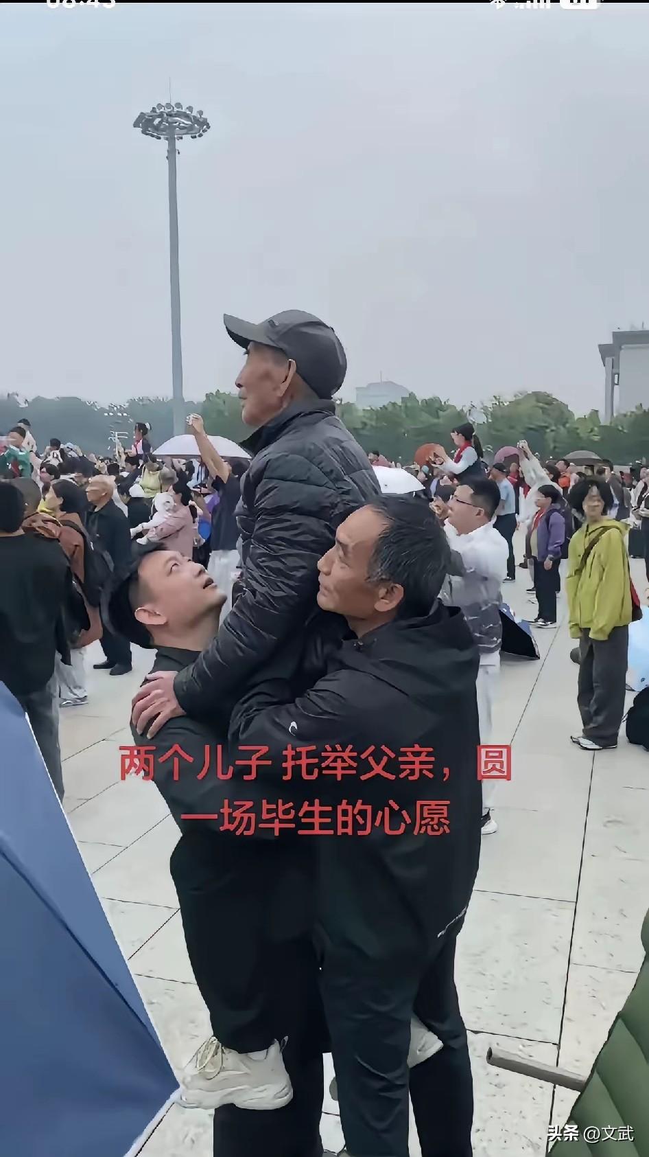 天安门广场升旗仪式，两个中年儿子托住八十几岁老父亲，合力把他举过肩头。刚好能看见