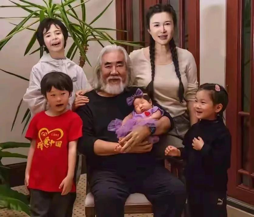 张导怀中的小可爱很惹人爱哦，像个紫衣小精灵一样乖巧地躺在老父亲臂弯里。一把年纪的