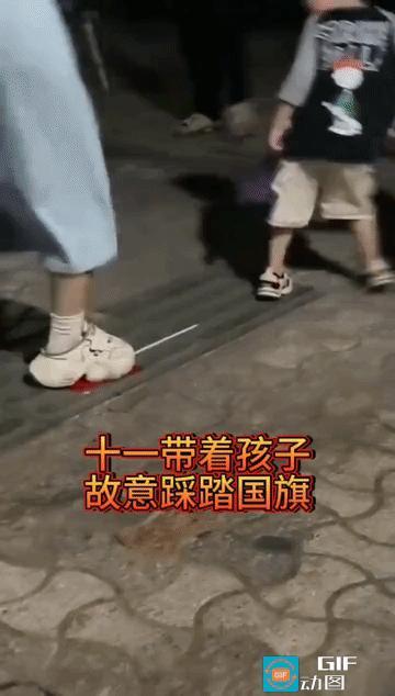 网友愤怒了:女子带一对儿女出门游玩，两个孩子手牵手走在前面，地上有一个国旗，但小