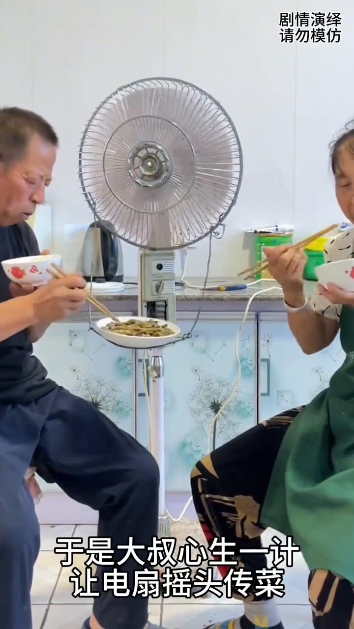 大叔巧妙用电风扇传菜来吃饭。
夫妻两个在吃中午饭，由于餐桌坏了，炒的菜没地方放，