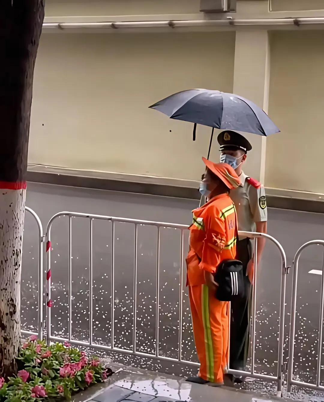 这是一位网友拍到的一位环卫大妈，为一位执勤站岗战士打伞的暖心镜头。鱼水之情的军民