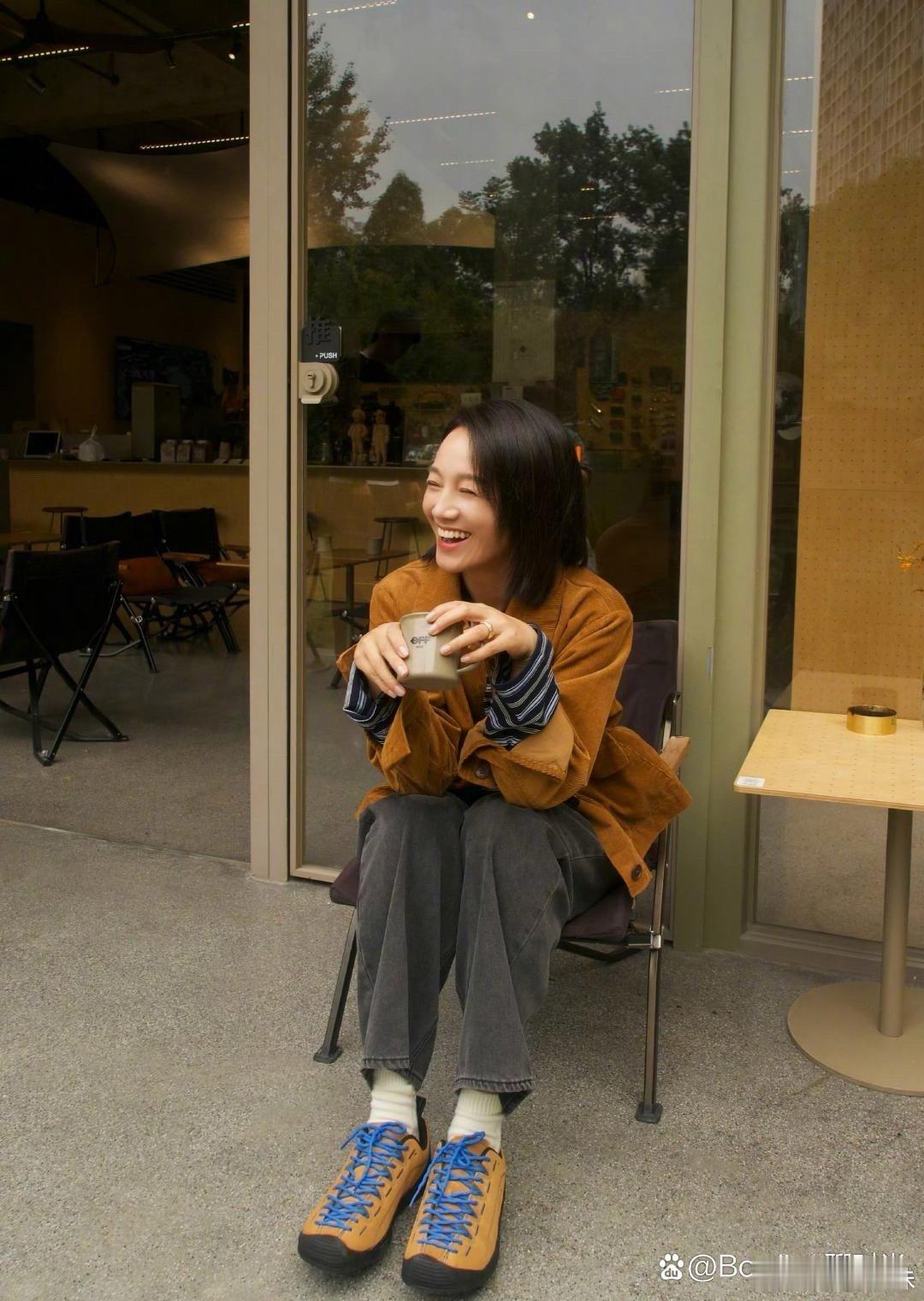 朱丹坐在咖啡馆外，手捧热咖啡，笑容温暖，享受着悠闲时光。 