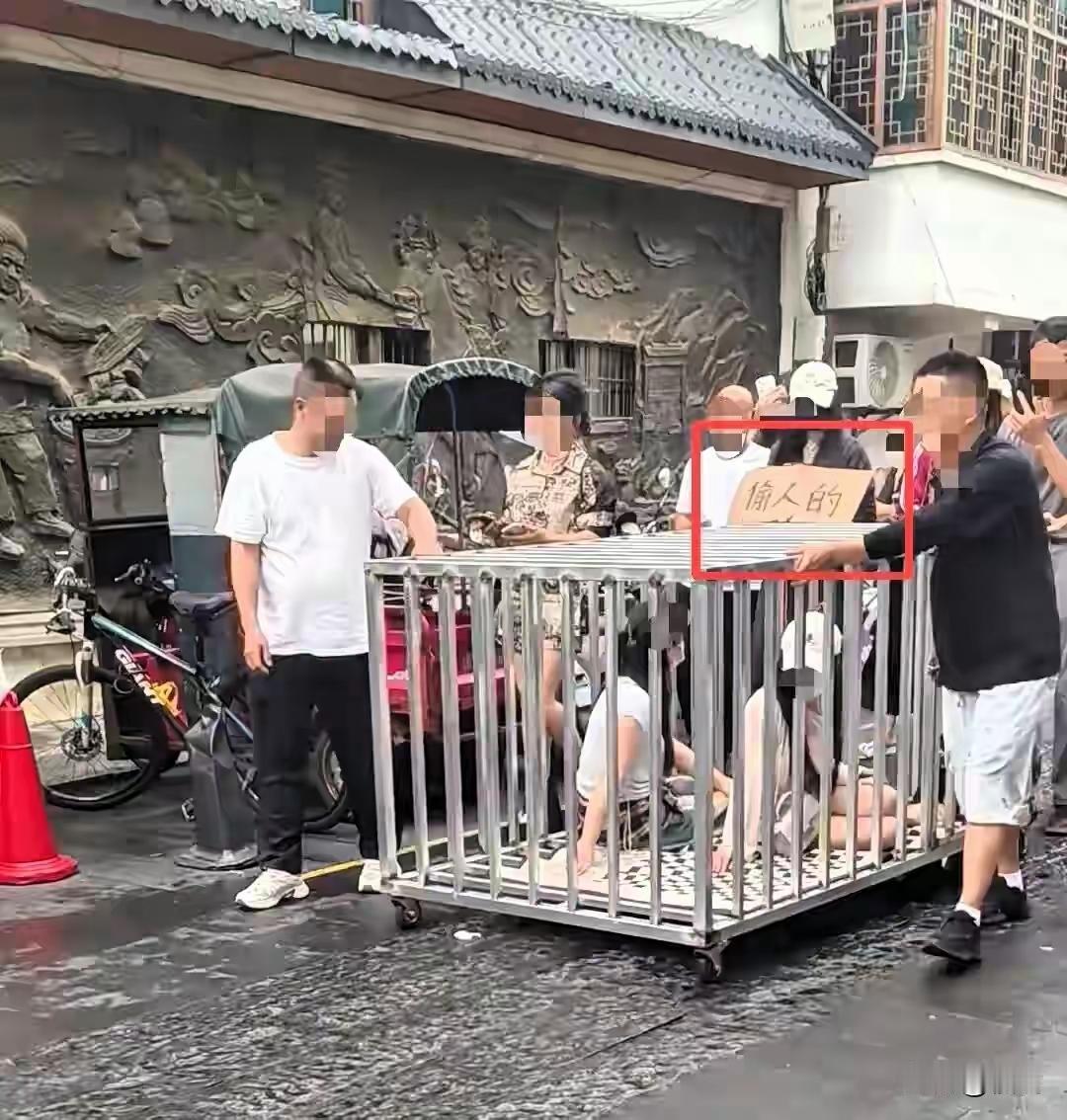 笼子上写着“偷人的”三个字，两女一狗挤进一窝，沿街被推着游行
 
湖南汨罗街头近