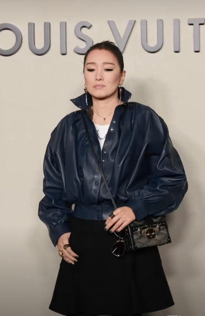 巩俐出席LV的某个活动，她身着‌深蓝色皮质外套‌，搭配黑色短裙与黑色短靴‌，手持