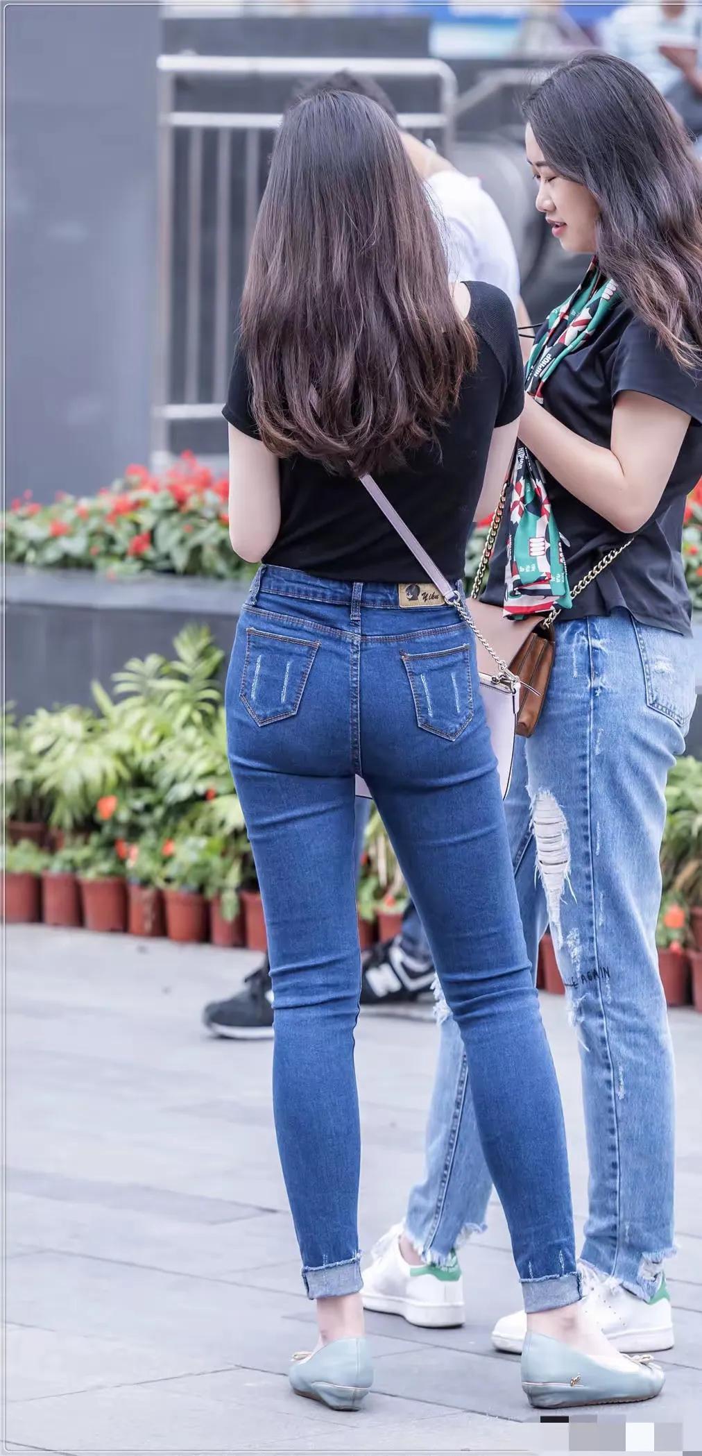 两位美女，她们均穿着黑色短袖上衣，下装为蓝色牛仔裤，不过款式有所不同。左侧女性穿