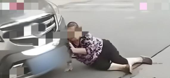2021年，辽宁沈阳，大妈看路边停放了一辆好车，用身体蹭上车灯，然后就躺在车前面