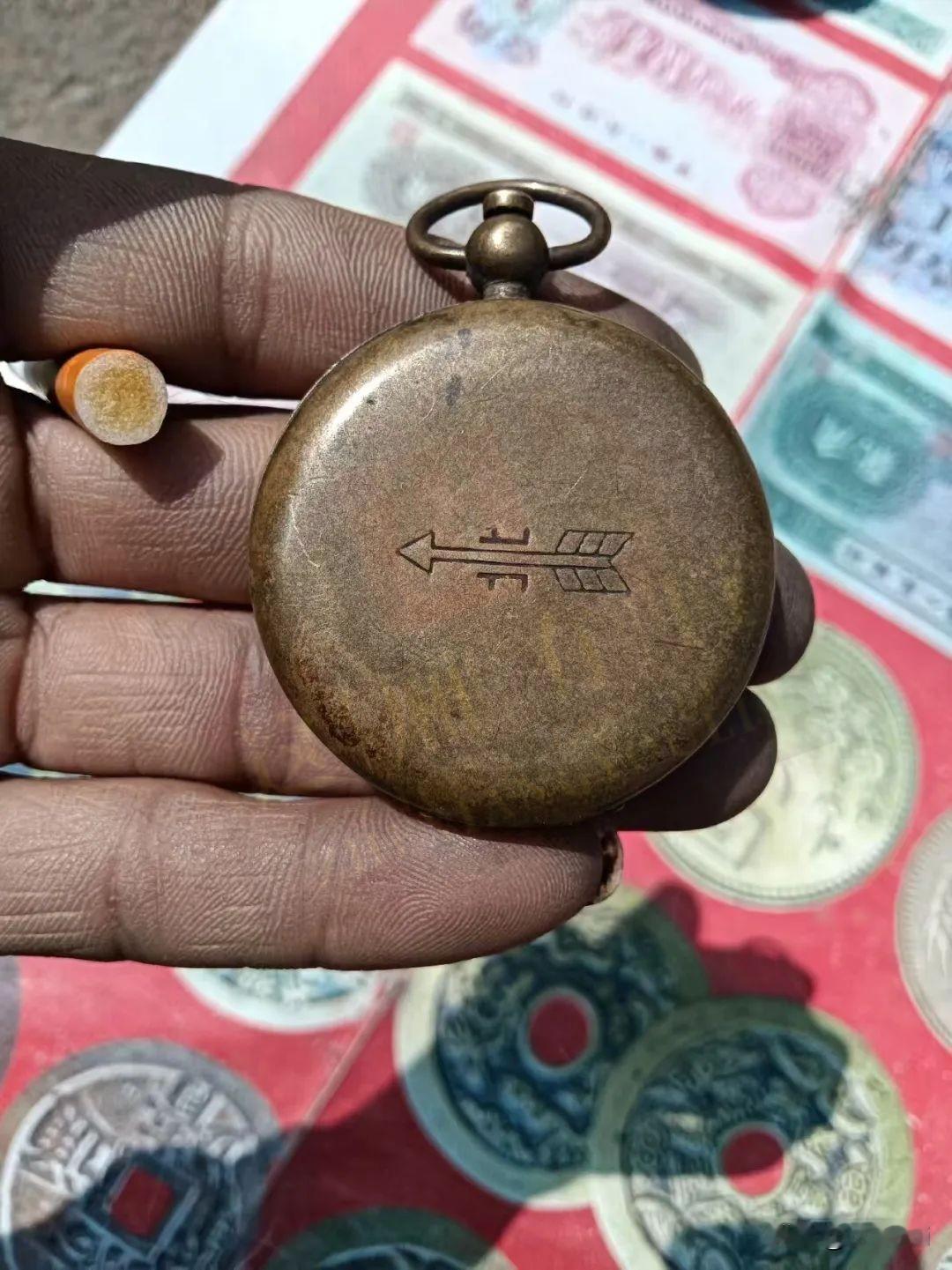 一枚饱经岁月的铜质老物件，外壳布满时光留下的斑驳包浆，背面刻着独特箭头纹饰。在过