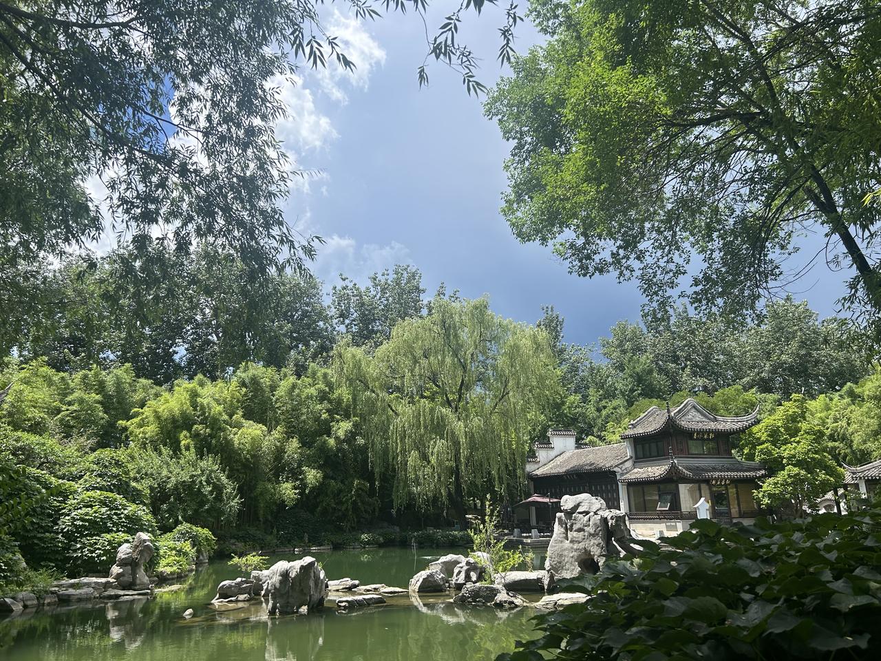 这哪里是照片，分明是一幅活过来的水墨丹青。柳丝垂烟，池水如碧，亭台山石都浸在温润