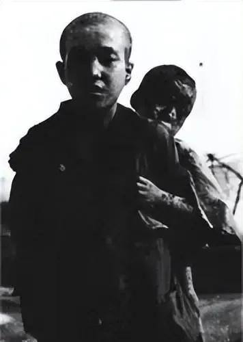 1945年，一名10岁的日本男孩抿着嘴，笔直地背着弟弟。而弟弟头向后仰，早已气绝