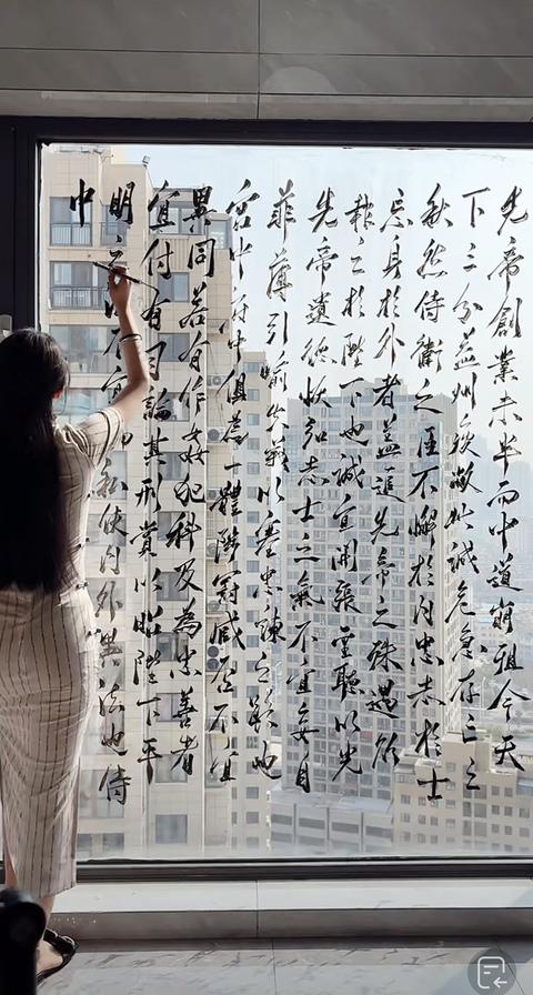 身穿旗袍的美女，在落地窗上用毛笔写《出师表》，感觉写的还挺不错的。

书法