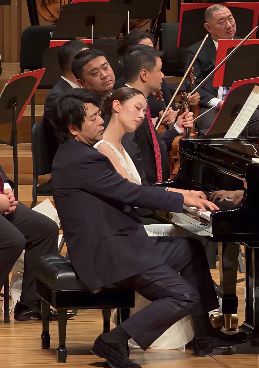 昔日，郎朗与吉娜在现场与多种乐器交响演奏的画面。

夫妻俩闭着双眼演奏钢琴曲，已