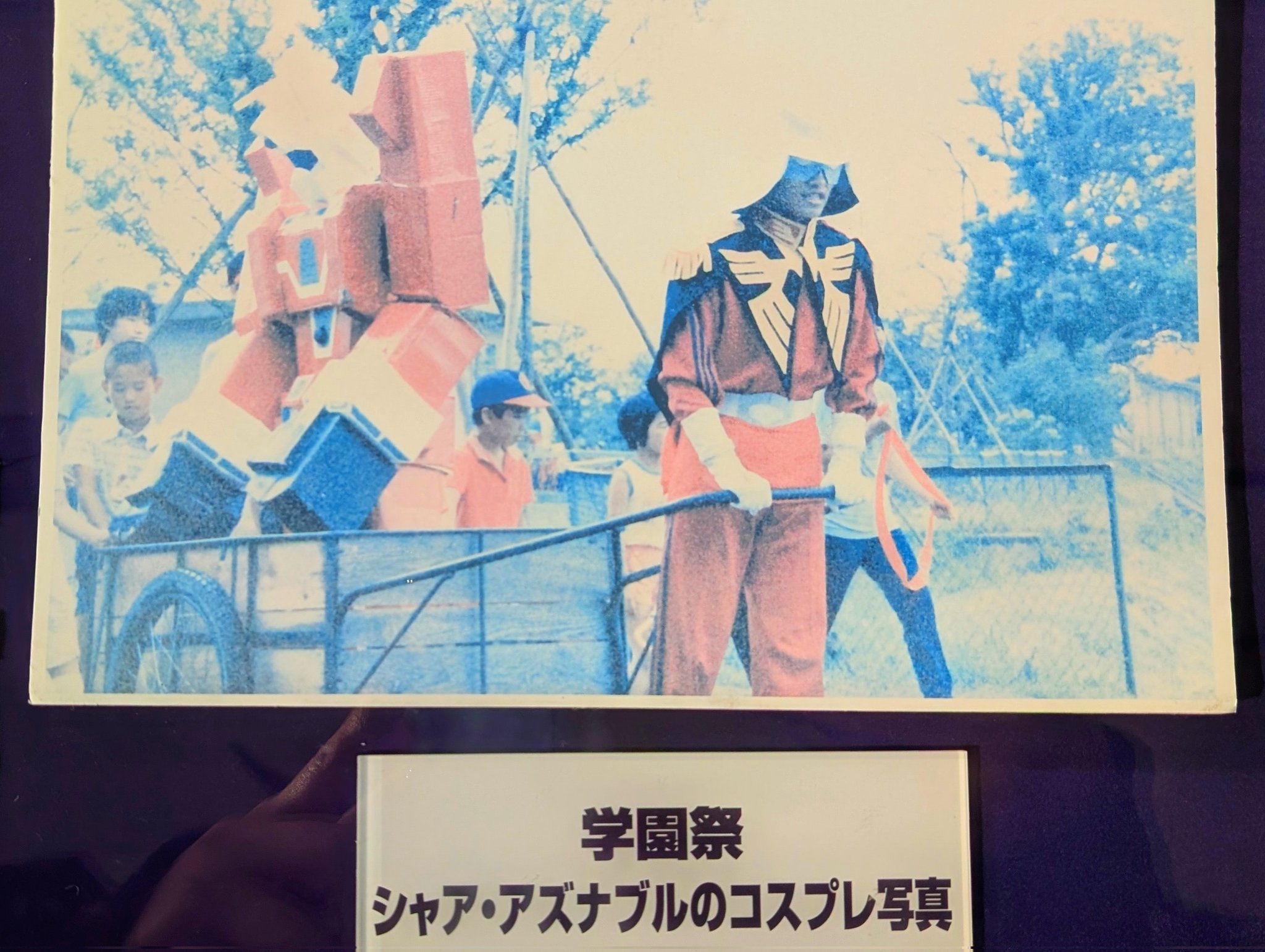 青山刚昌资料馆中的展出一张照片，在学院祭上青山刚昌扮演夏亚，用板车拖着传说巨神伊