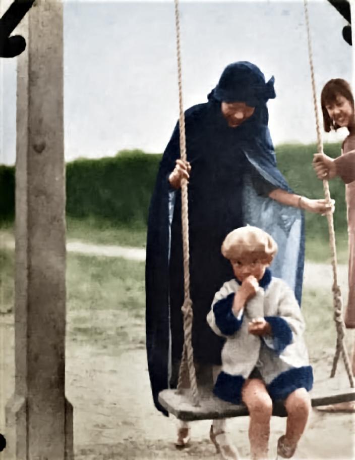 这张照片里，婉容裹着深色长披风、头戴软帽，和一个孩童同坐秋千板上，她微微俯身，神