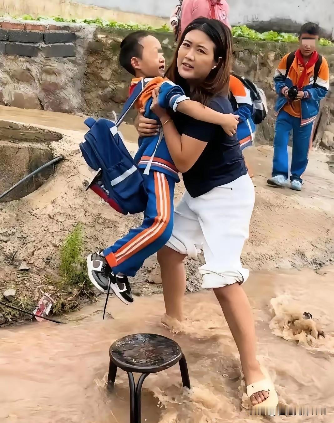 一大早，女子高高挽起裤腿，趿拉着拖鞋就站进水流湍急的小河里，把岸边的学生从这头送