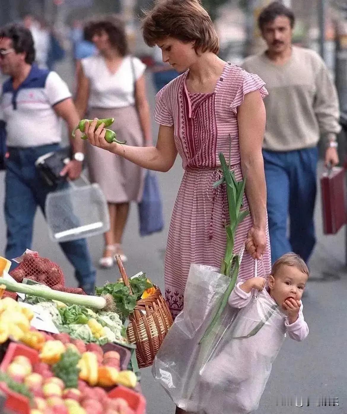 80年代，一位母亲用塑料袋拎着她的女儿去买菜，孩子和大葱放在一起。不得不说，这个