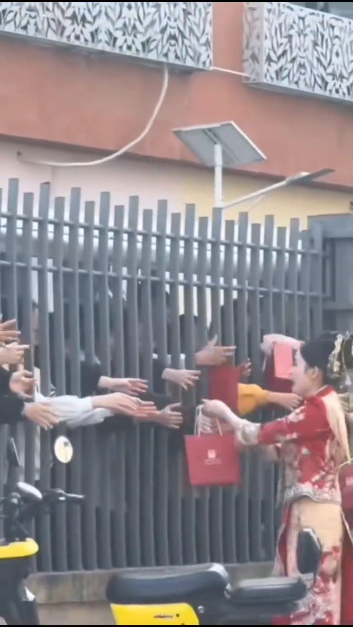 婚车路过学校偶遇学生下课，孩子们趴在围栏上"硬核"送祝福，新人狂送喜糖分享喜悦。