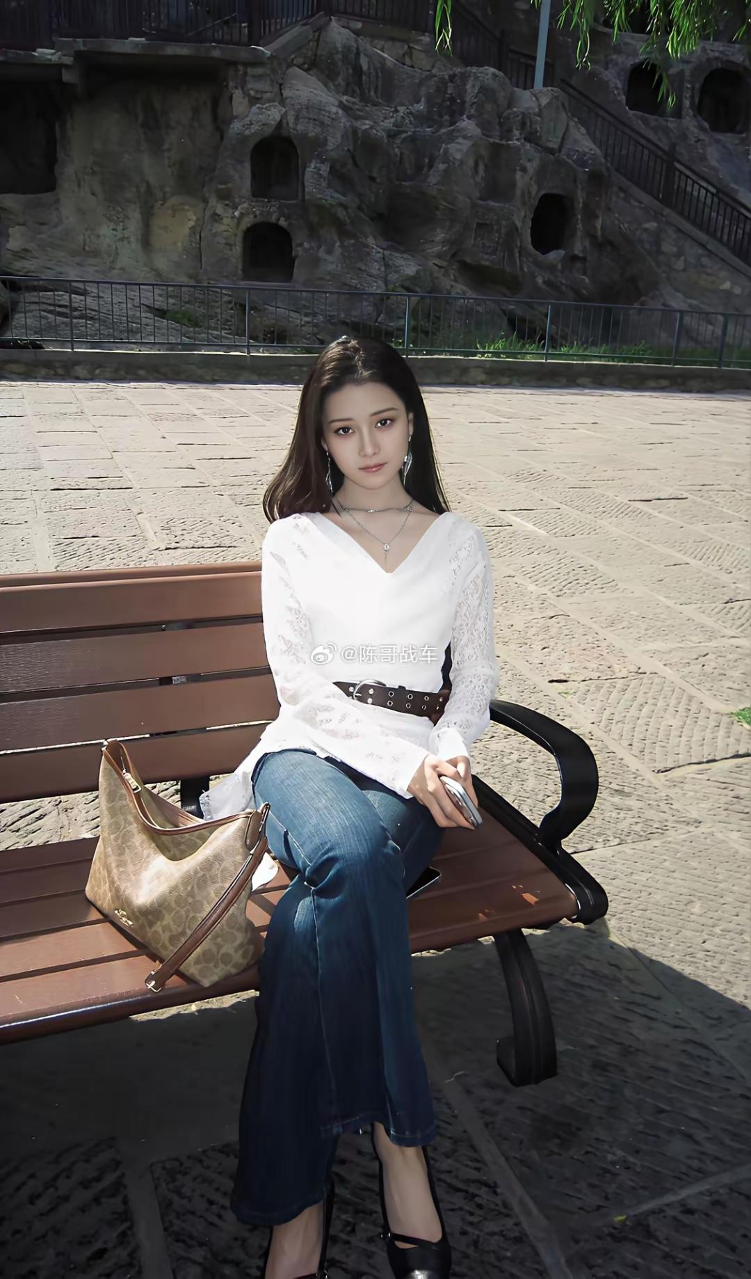 美女坐在公园长椅上，手拿手机。