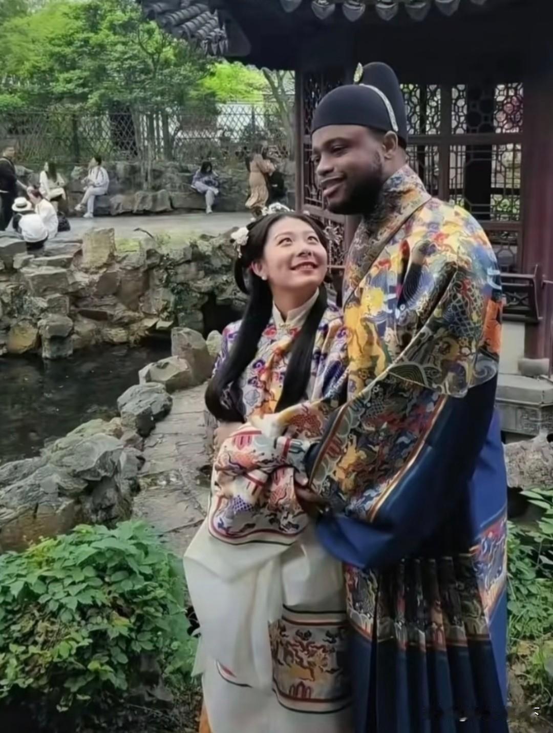 一对情侣在中国古典园林穿着古装拍照，男子身材高大，皮肤黝黑，看上去像是一个典型的