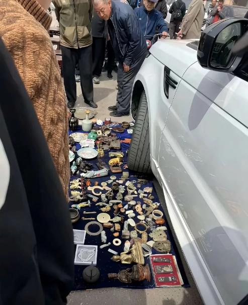 古玩地摊刚铺开，路虎一个车轮直接压到满摊古董。 一圈大爷瞬间围上来，全都弯腰仔细
