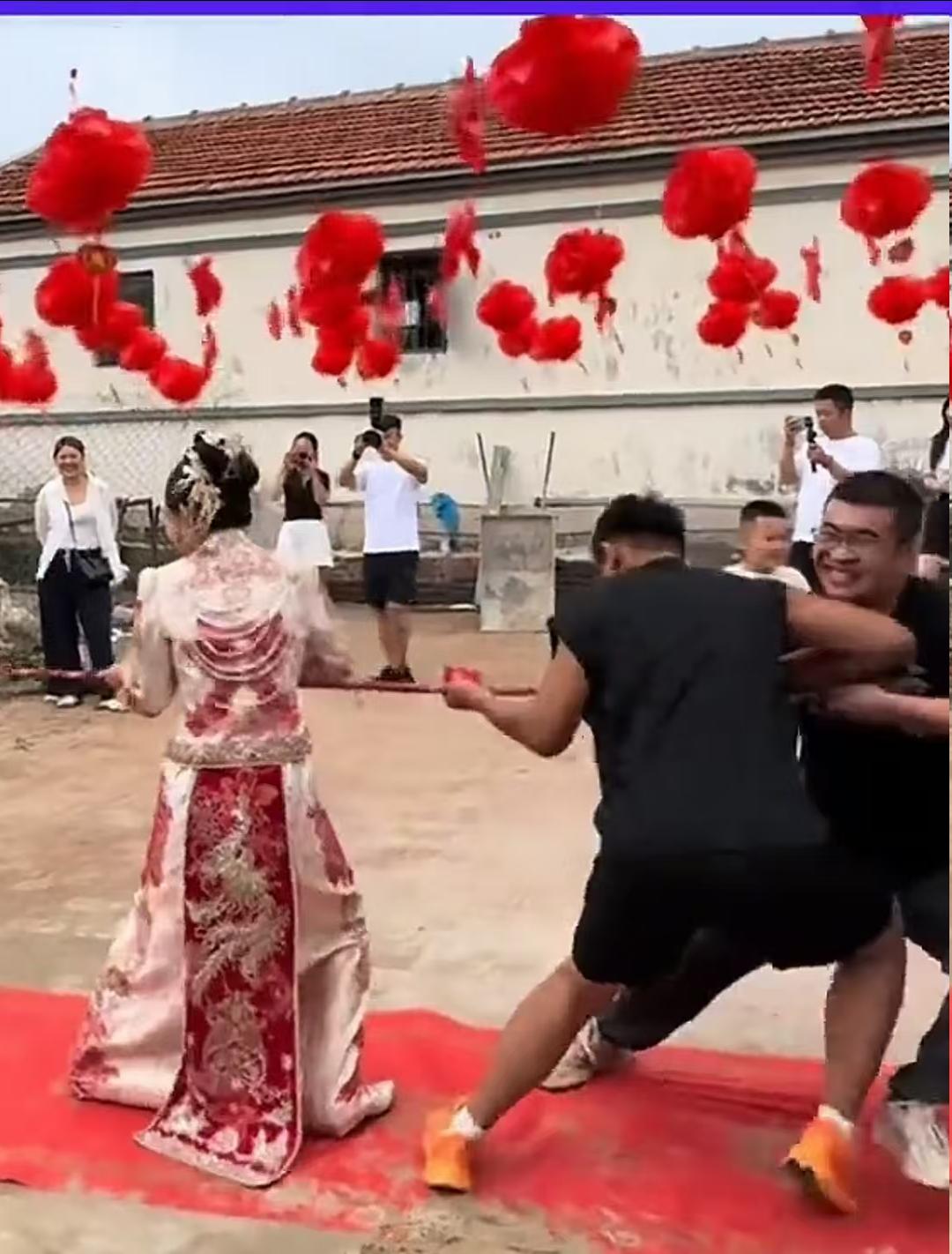 有意思，现在结婚不玩藏鞋堵门这一套了，竟然当众进行了拔河比赛。

只见绳的一头是