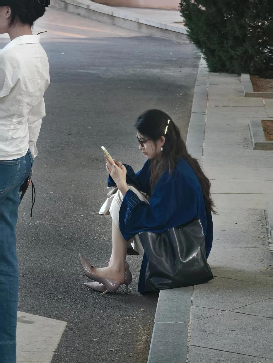 一位女士坐在路边看手机。