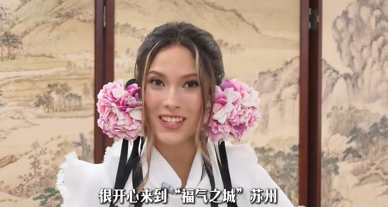 谷爱凌把耳畔的粉色大花，戴进了苏州的会见现场。白裙、花饰、黑色飘带，和人们印象中