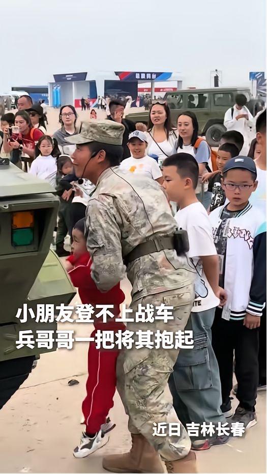 吉林，一个小男孩走到坦克战车前，踮起脚想爬上去可却只能够到轮子，旁边的兵哥哥一把