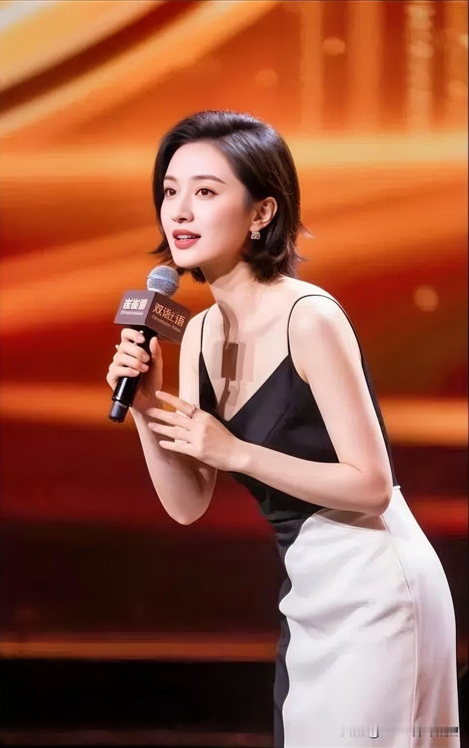 聚光灯下，黑白裙裾勾勒出曼妙风姿。执麦轻诉间，流转着知性与从容。眸光熠熠，宛如一