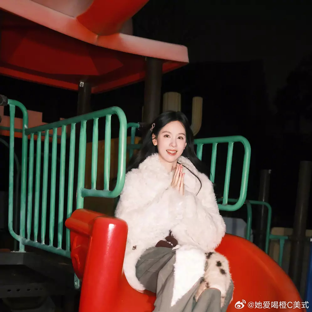 陈都灵穿白色外套，别着发卡，在滑梯旁拍照，灵动活泼。 