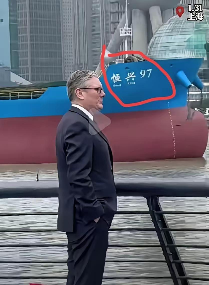 英国首相斯塔默到上海外滩打卡，穿西装打领带站在黄浦江边，背后“恒兴97”号货轮缓
