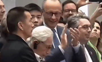 仔细看，德国总理默茨在看人形机器人表演时，在鼓掌时，有好几次侧脸望向陪在他左手边