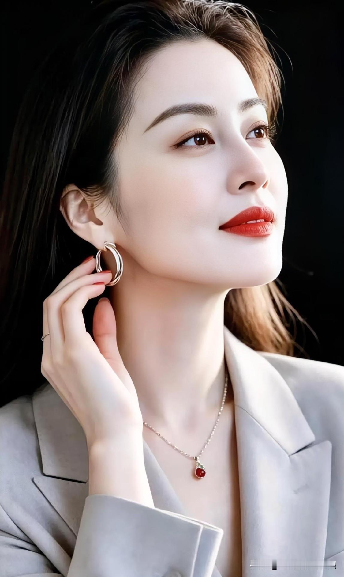 浅灰西装勾勒出优雅的轮廓，红唇微启间尽显从容气度。指尖轻触发丝，温润的红豆吊坠点