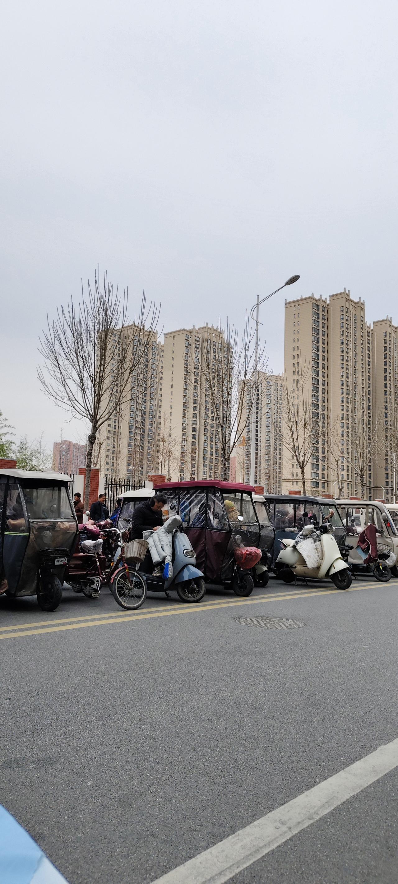 清晨的街道边，一溜儿停着各式的电动三轮车和电动车，车身上搭着厚外套、挂着菜篮子，