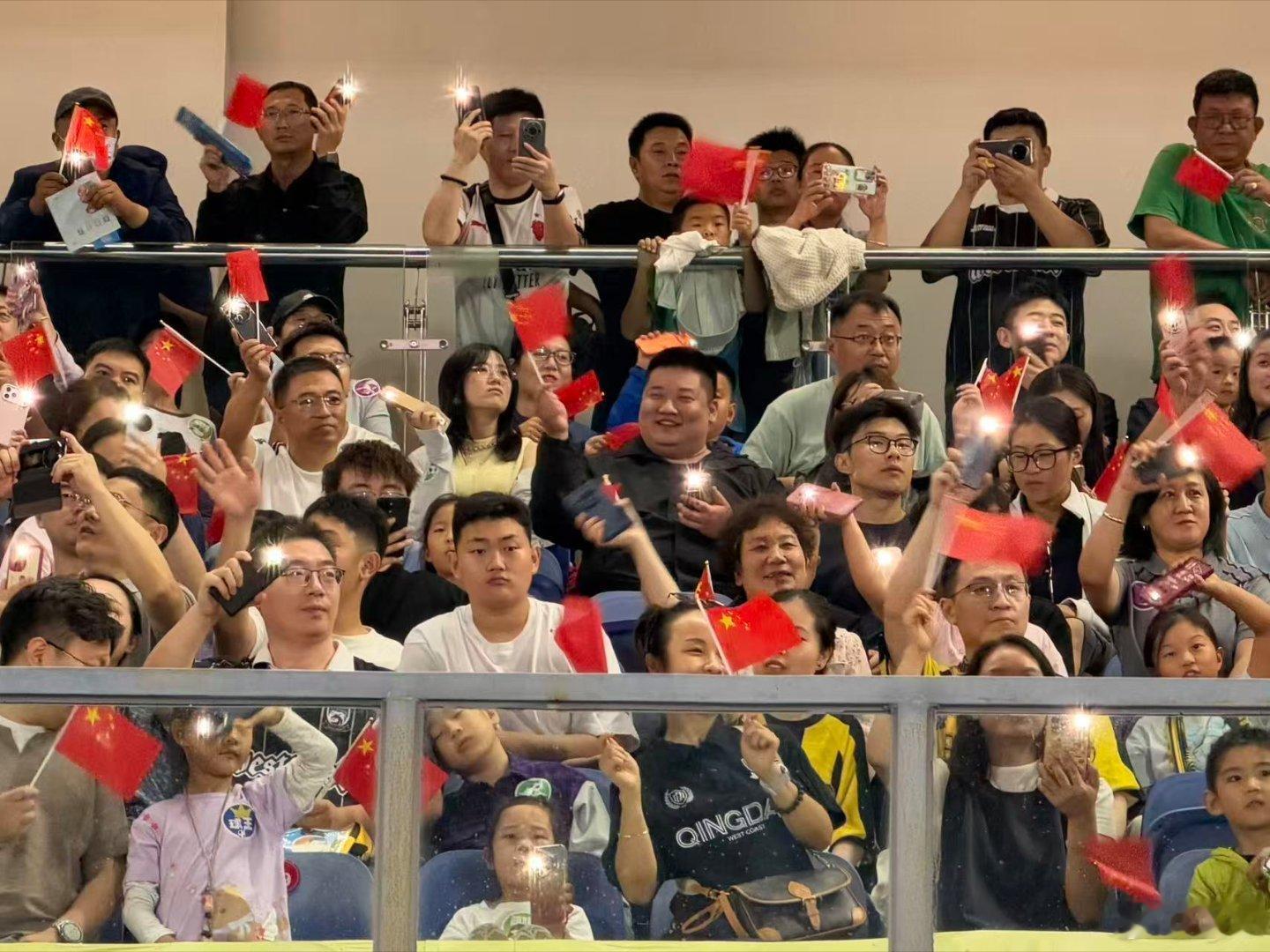 青岛城市足球争霸赛正式开赛，球员们在赛场全力奔跑对抗，观众席欢呼声此起彼伏，赛事