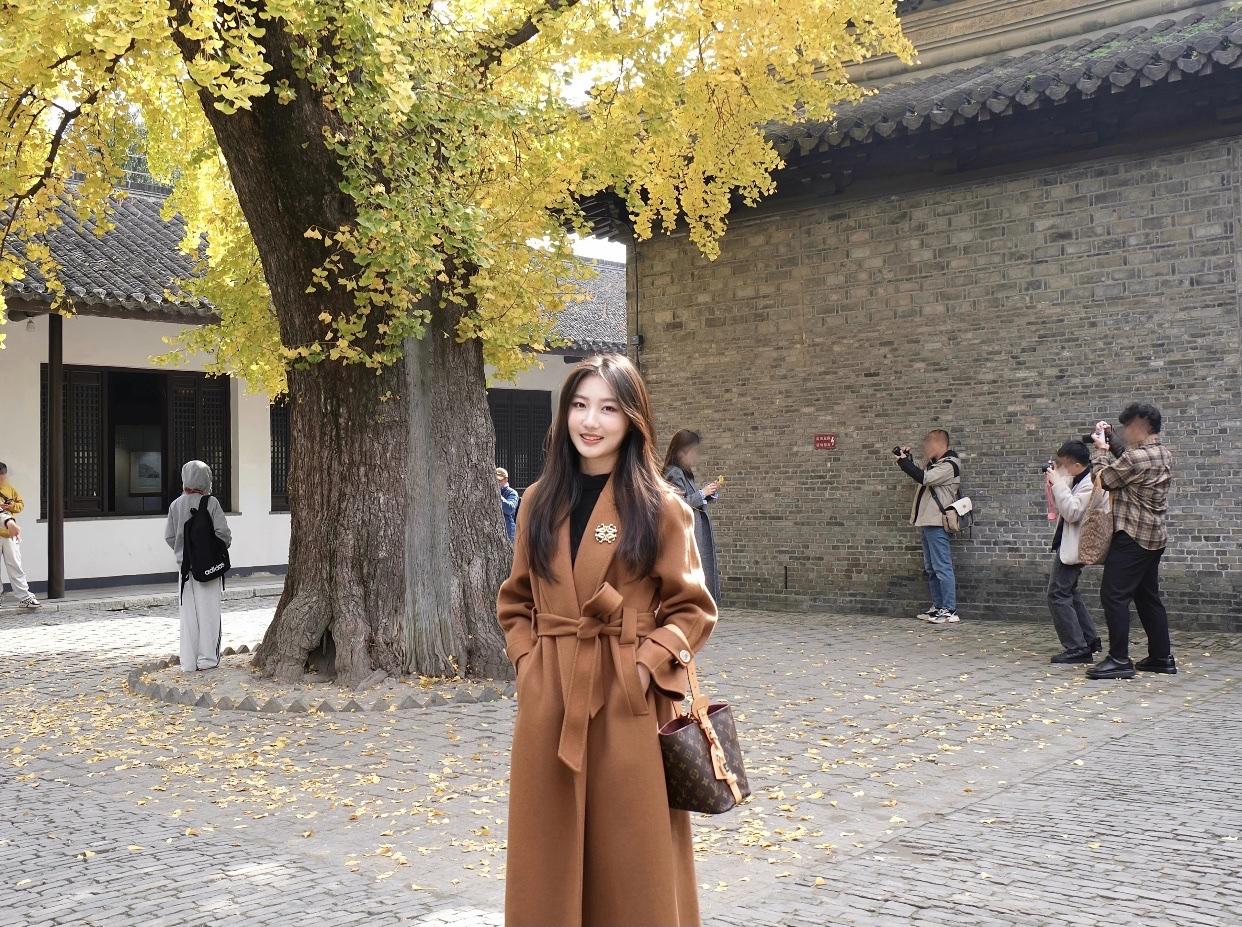 秋日暖阳下，优雅的棕色大衣与银杏叶相映成趣，尽显温柔与浪漫。