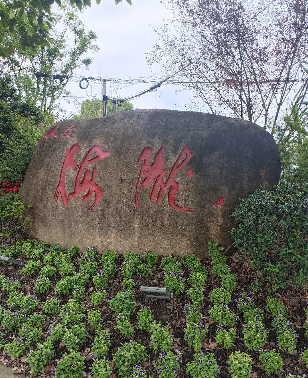 花坛里立着一块刻着“梅陇”二字的石头，旁边盛开着几簇不知名的小花，红的黄的挤成一