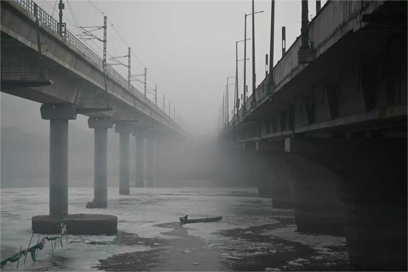 下面这张图是印度首都新德里的亚穆纳河。
图中一名市政工人在浓雾中乘坐小船，在冒着