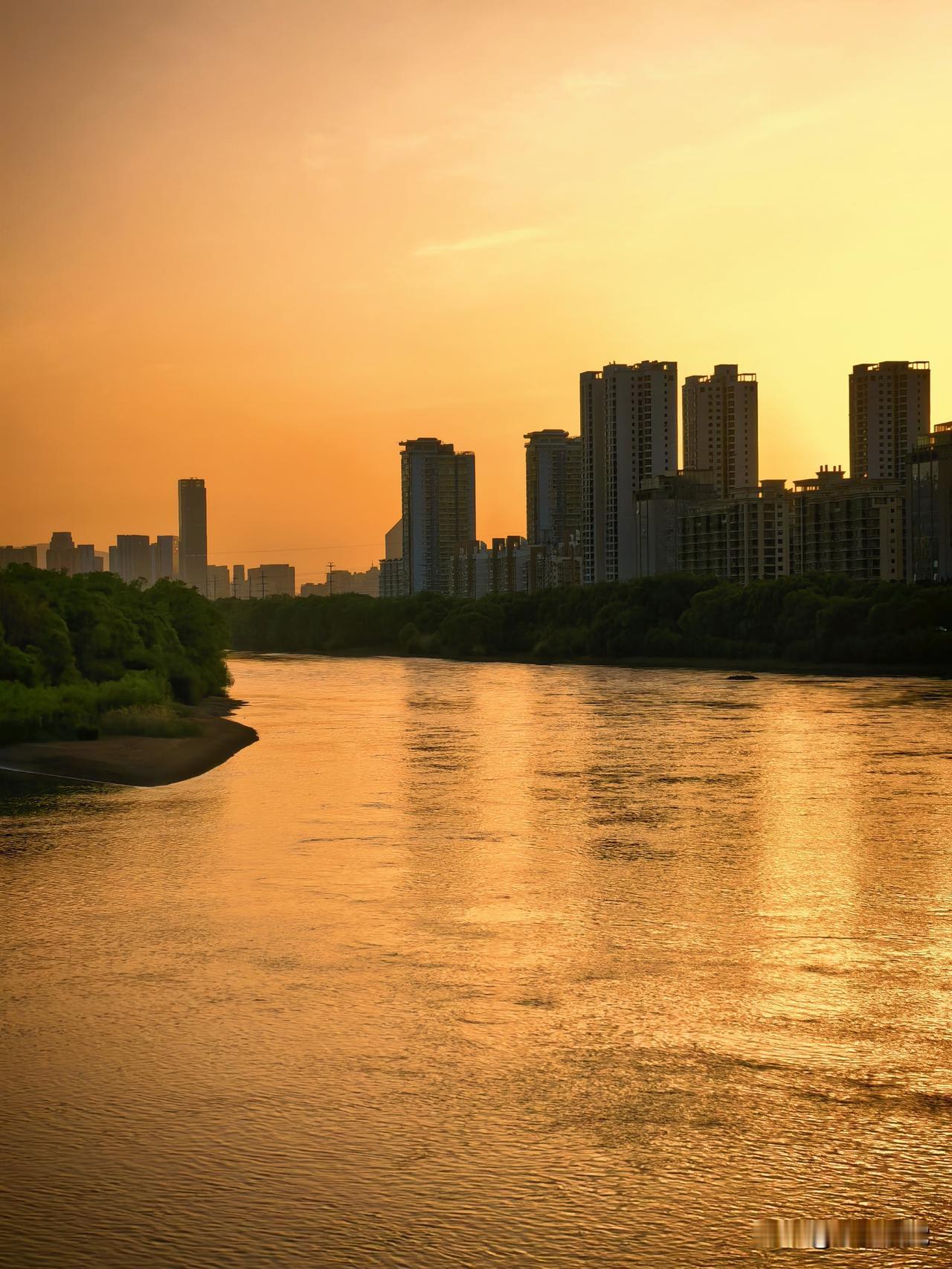 西部摄影落日熔金漫大河，余晖铺浪漾金波。长堤翠树围河岸，静泊孤舟枕晚歌。一城楼宇