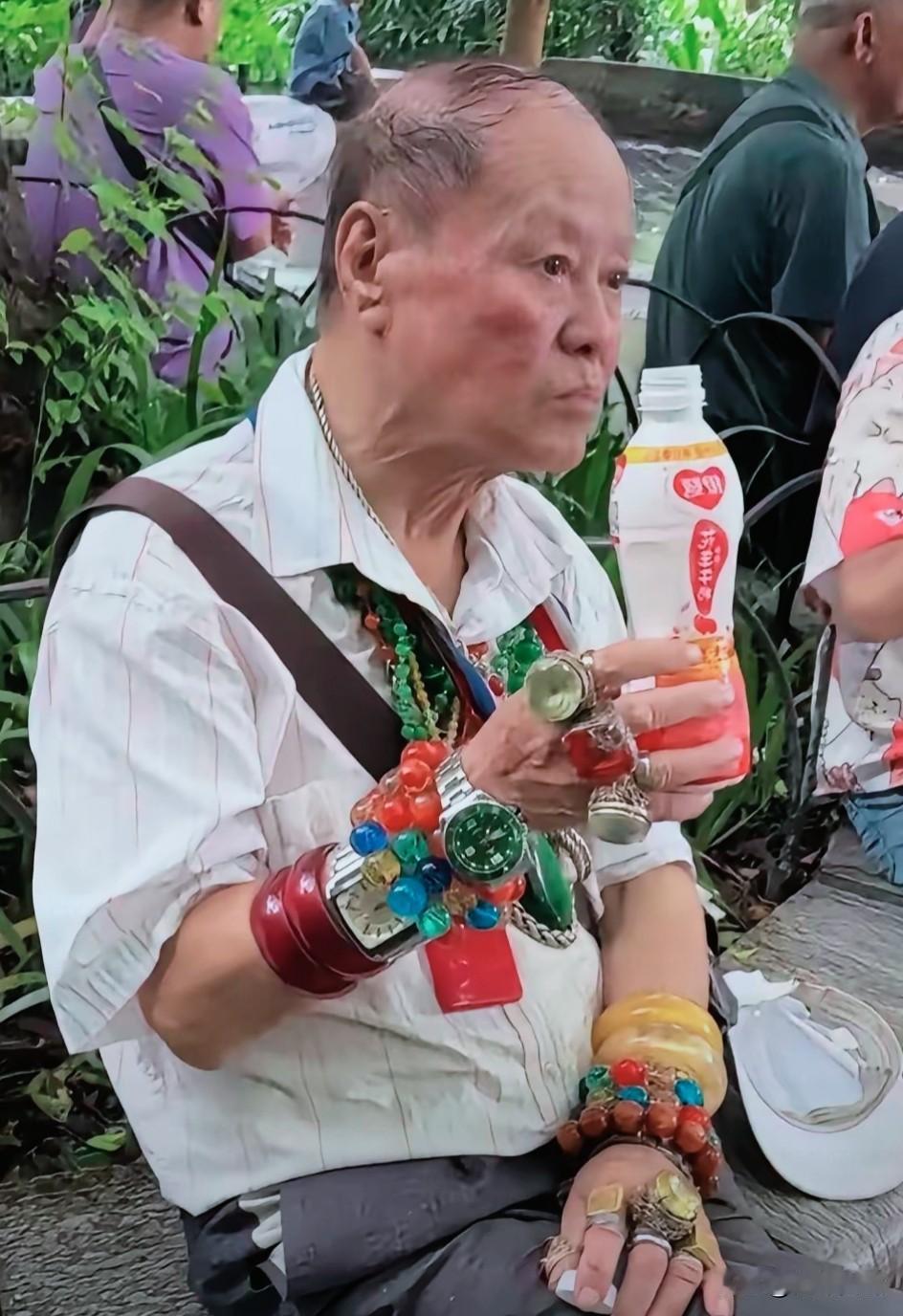 像极了资深老炮儿。
不过，除了他手里的那瓶饮料看看像真的，手臂上戴的、脖子上挂的