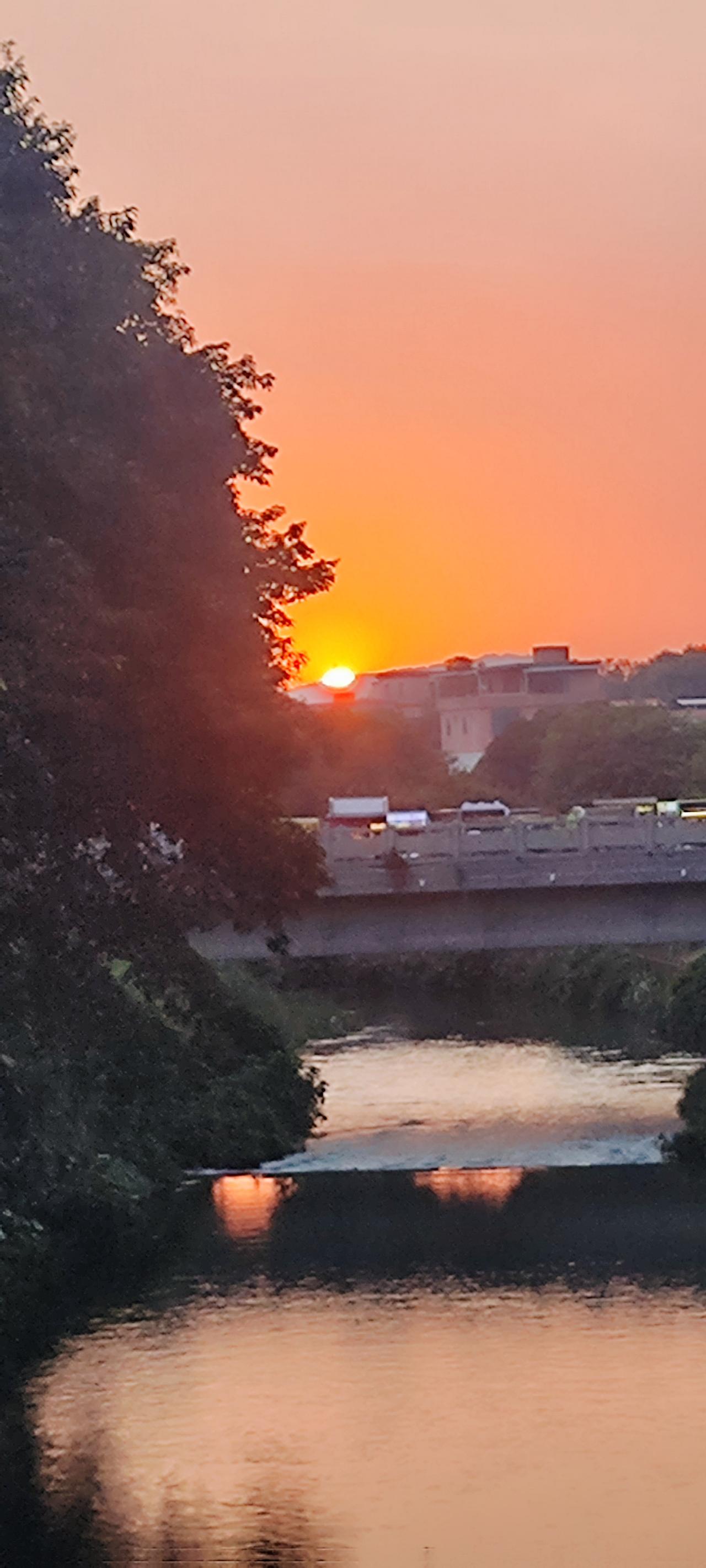 站在广东东莞清溪镇的清溪河桥上望去，夕阳西下，霞光万道。火红的太阳靠着山边缓缓西